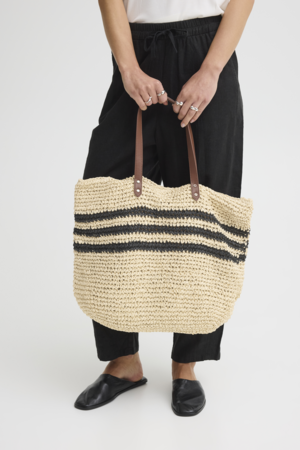 Shopper tas natural in handen gedragen bij zwarte broek outfit
